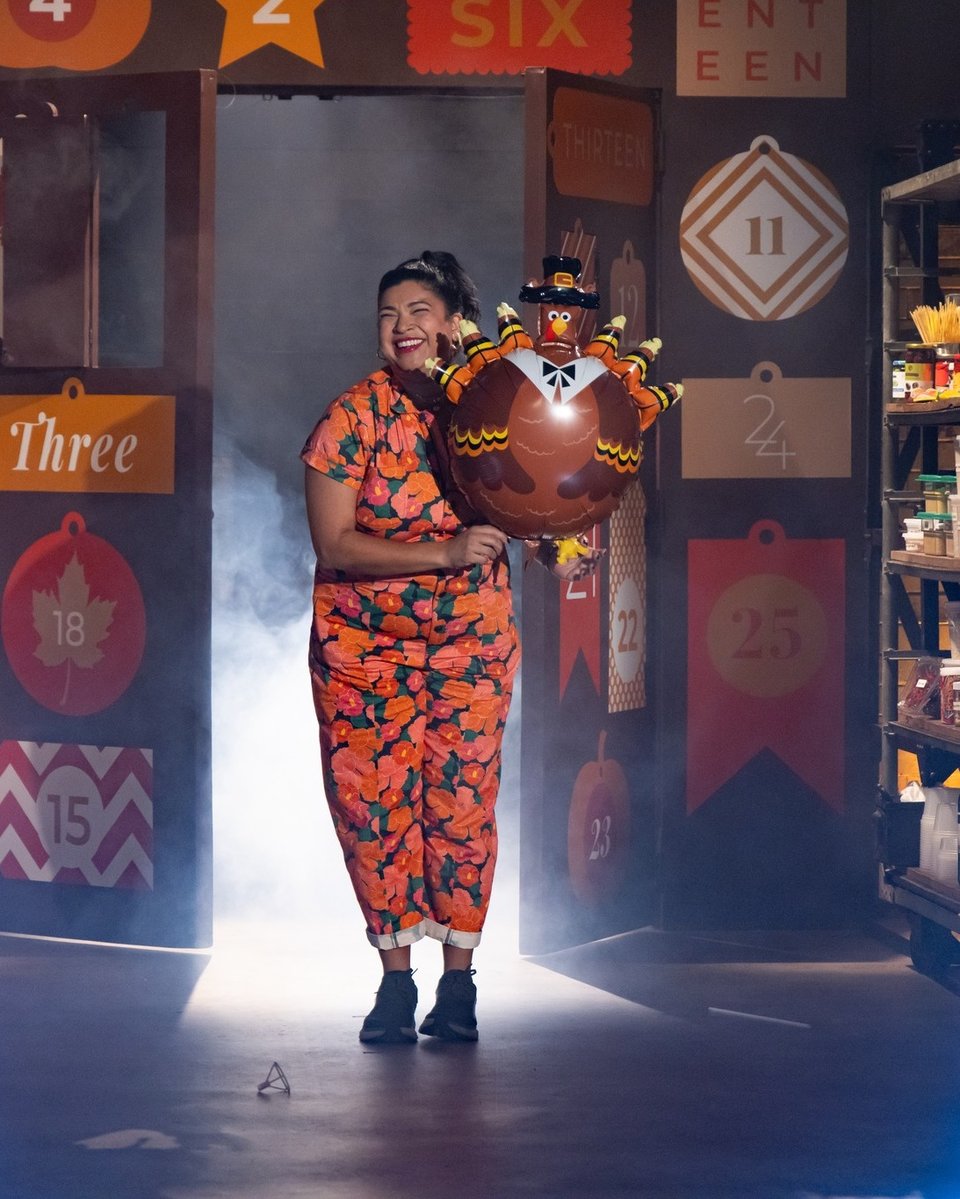 a woman in an floral orange jumpsuit holding a large turkey-shaped balloon