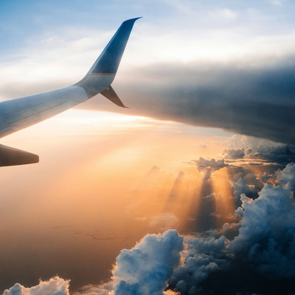 Tail section of a plane flying through a sunny sky with clouds