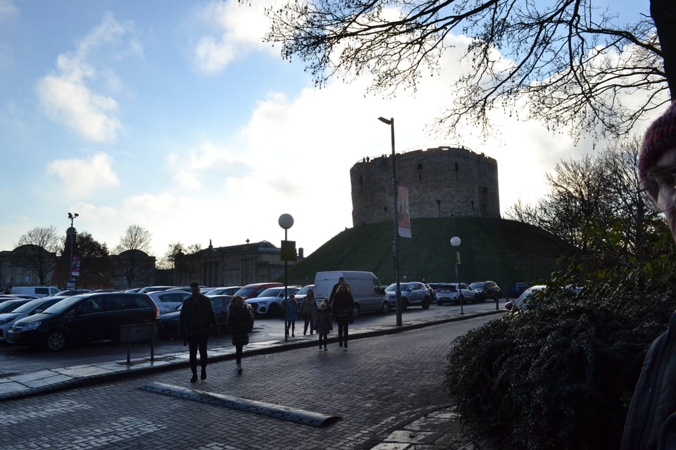 A tower on top of a mound broods over a parking lot.