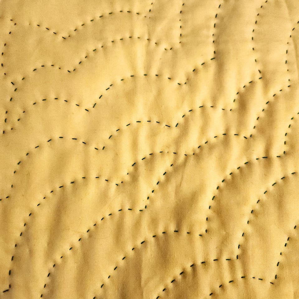 Photo of the back of Sunshine Spreads a Carpet showing yellow fabric and curved lines of hand stitching.