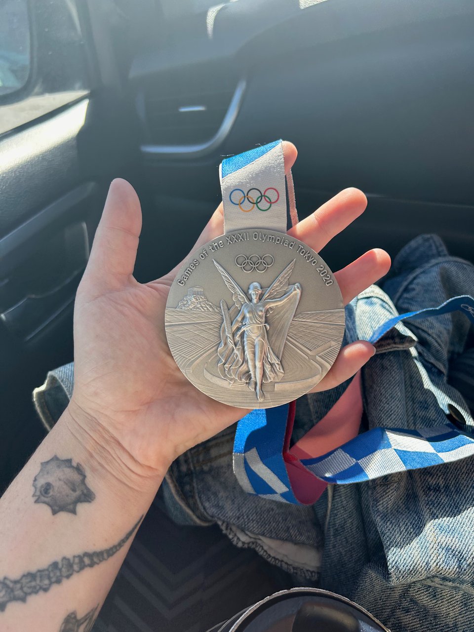 A hand holding an Olympic silver medal, which has a woman with wings on the front and says "Games of the XXXII Olympiad Tokyo 2020"