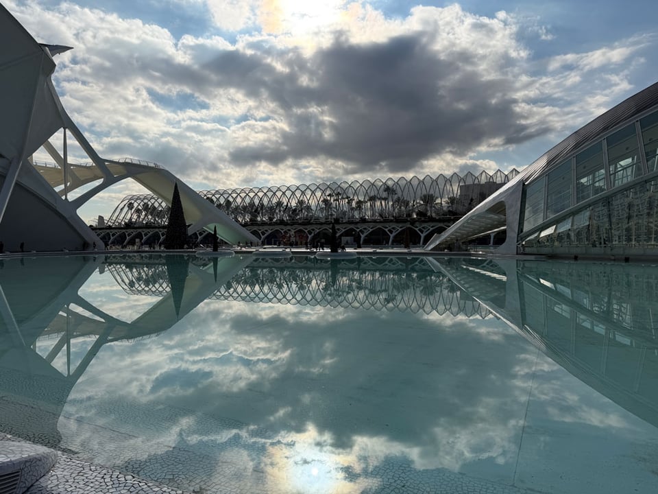 Architecture with a body of water in front reflecting the clouds and the sun.