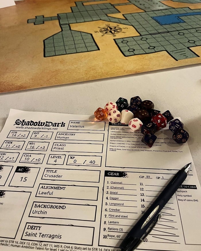 My Shadowdark character sheet on a table, with a pen and some dice, and the edge of a game map visible.