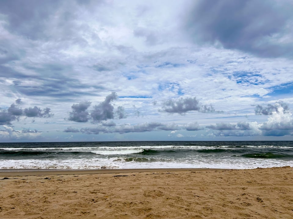 Horizon view of a sandy beach with ocean waves and dramatic clouds in the sky