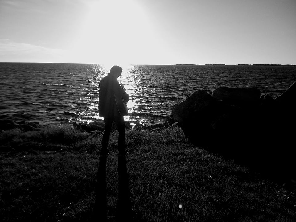 shane playing his guitar into the sun over the ocean