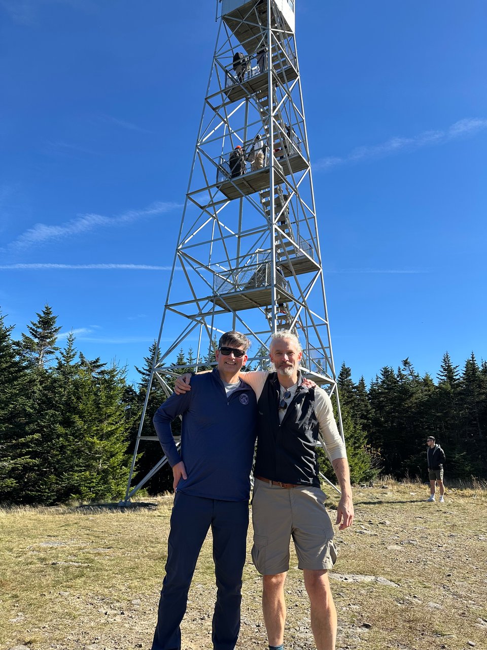 photo of 2 white men in front of Hunter Mountain fire tower in the Catskills; they each have an arm over the other's shoulder