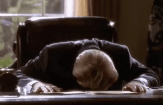 This is the classic "headdesk" gif: A man sitting on a chair and pounding his head on a desk as if deeply frustrated.