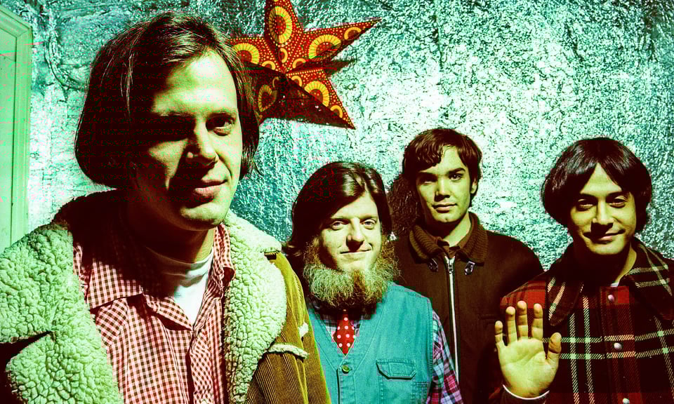 The four members of Neutral Milk Hotel (from left: Jeff Mangum, Scott Spillane, Jeremy Barnes, and Julian Koster) standing in front of a sea-green colored wall with a red and orange star hanging behind their heads.