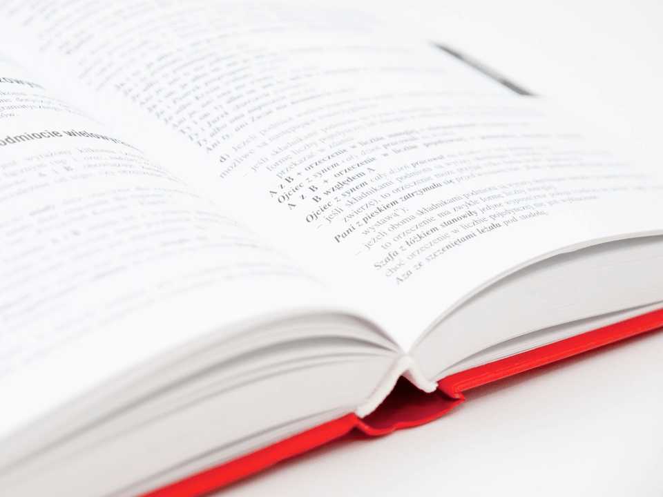 A hardcover book, with a red spine, opened and lying on a white table. The photo is so high-contrast that we cannot easily read the bright, blown-out text