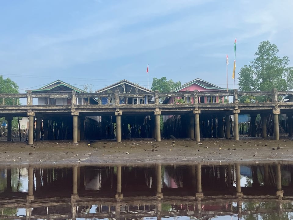 three houses built on a jetty over a river as seen from the river at low tide
