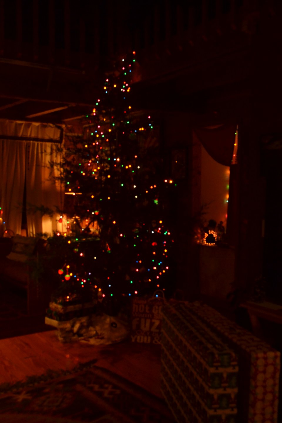 A decorated, tall Christmas tree in the corner of a room with presents under and around it.