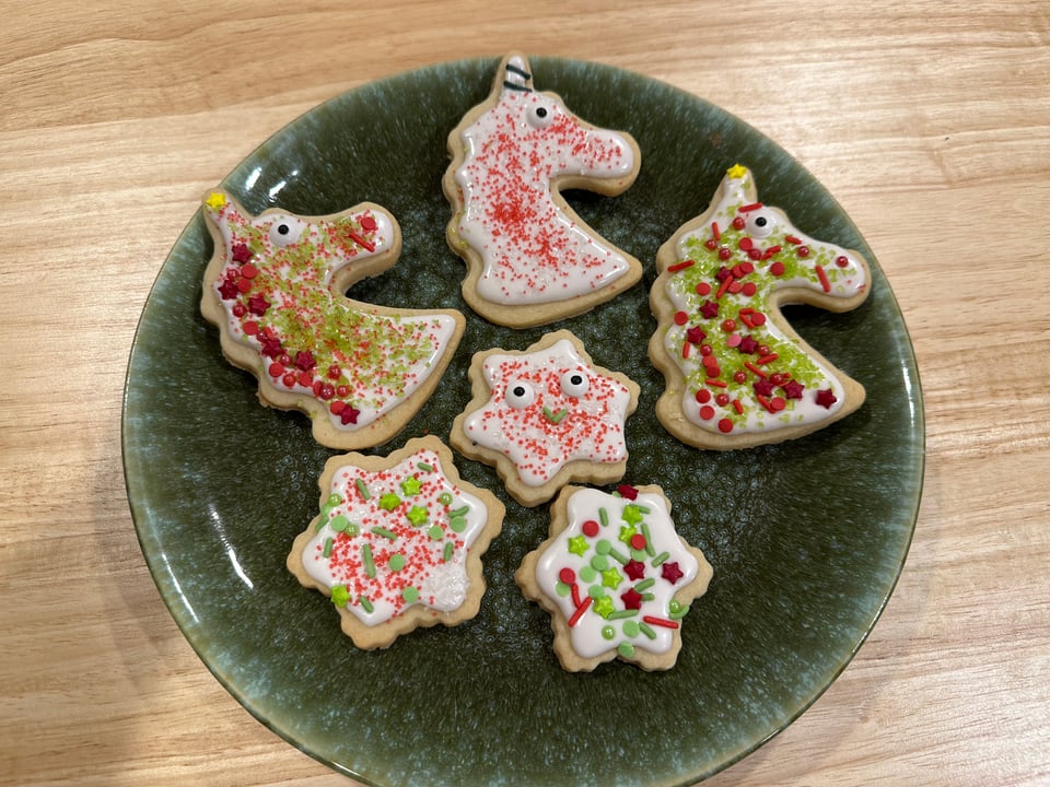a green plate with Christmas cookies in the shape of unicorn heads and Snowflakes with random sprinkles heaped on and some candy eyes