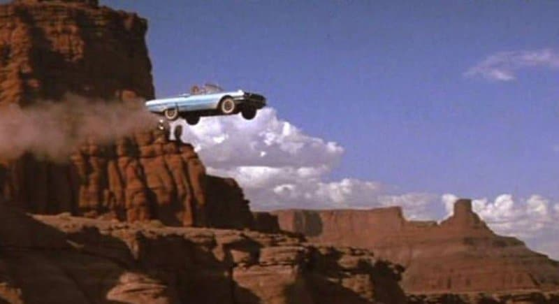 a car flies through the air as it leaves the edge of a cliff, perhaps it's Grand Canyon, the sky is blue, a few white fluffy clouds