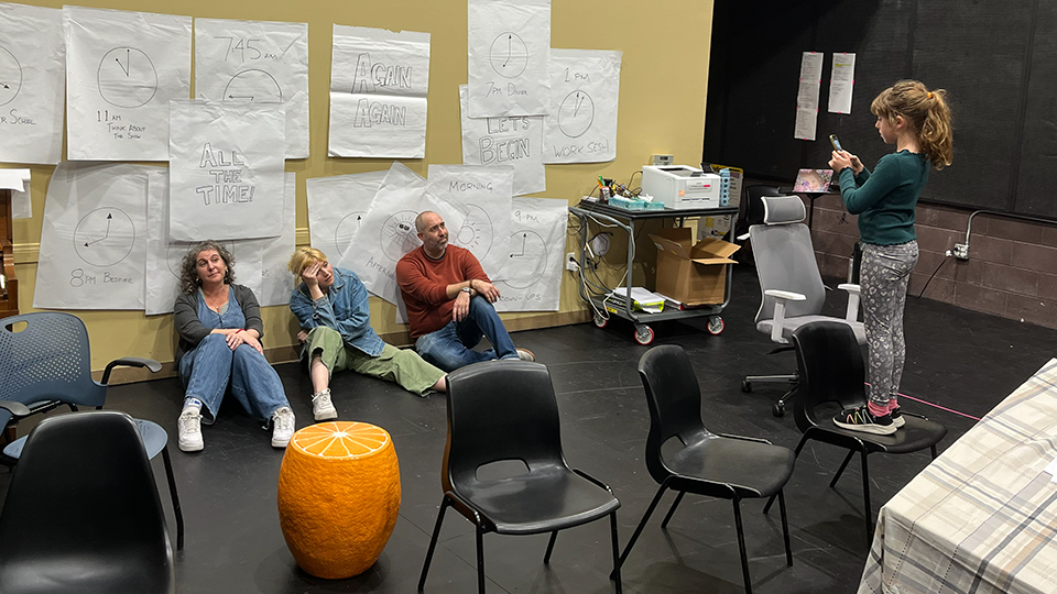A child stands on a chair taking a photo of three performers tired from performing.