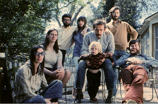 Seven adults and one child look at the camera. They are filmmakers from the 1970s. The men all have varying degrees of facial hair and the women all have long hair.