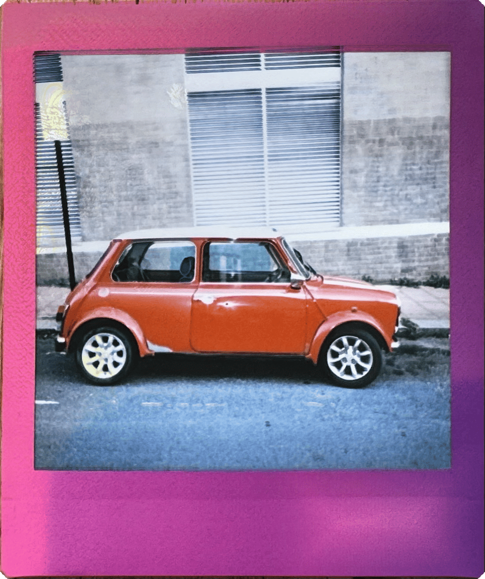 instant camera picture of an old red mimi cooper parked on the street.