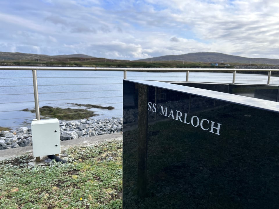 A close-up of the "prow" of the SS March monument in Lochboisdale, South Uist. The prow is black slate and reflects the fence leading to the bay.