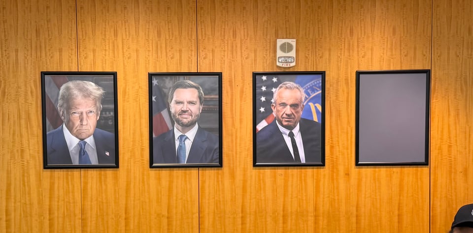 photo of wall behind security desk at bldg. 1 at FDA HQ, feat. 4 framed photos of the president, vice president, HHS secretary, and FDA commissioner; the last frame is empty