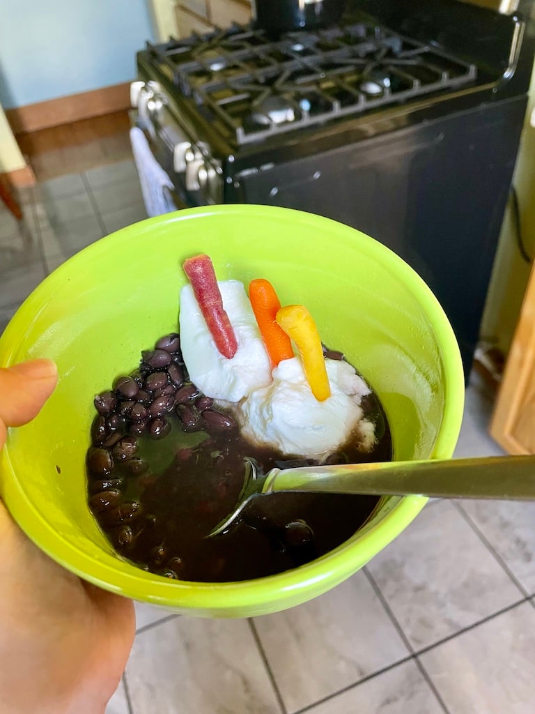 Turtle beans in a green bowl with a dollop of yoghurt and mini rainbow carrots