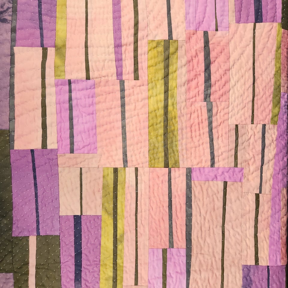 Detail view of Sarah Atlee’s patchwork quilt titled Arabesque I. The quilt is made from hand-dyed fabrics in pink, orange, grey, purple, and yellow green.