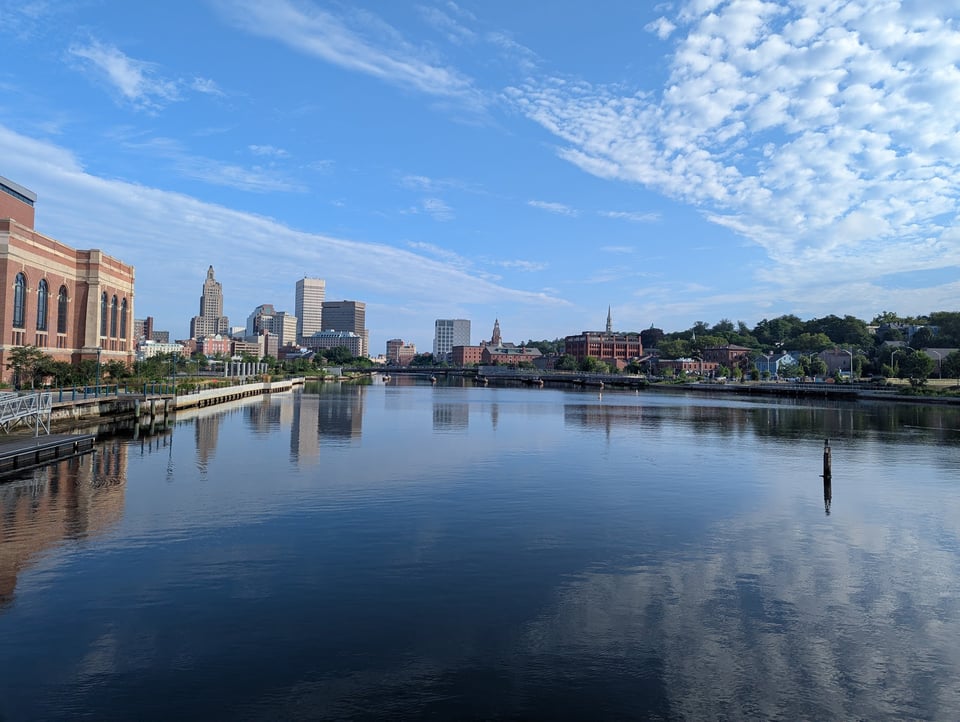 View of a cityscape and puffy white clouds reflected in a river