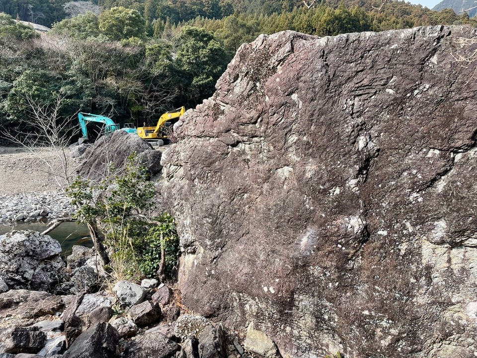 Warmup boulder with chalk prints by the Miyagawa river. Two construction cranes are in the background across the river. The left side of the boulder is bordered by a tree that is sturdy enough to use to assist the down climb.