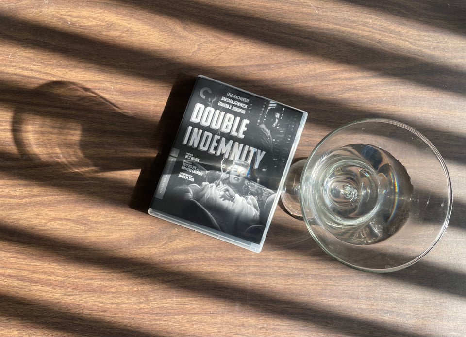 A martini and a Blu-ray of the film Double Indemnity on a table with dramatic, noir lighting