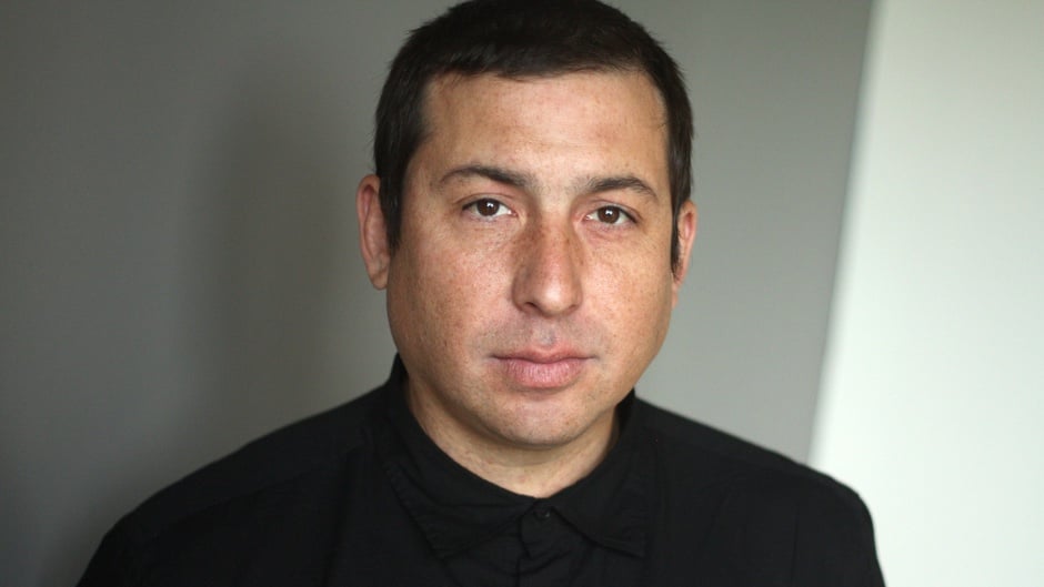 Photo of author Tommy Orange from the shuolders up, wearing a black shirt in front of a neutral background