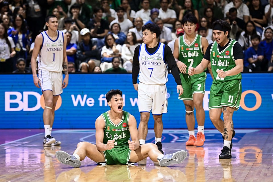 a filipino basketball player roars in celebration while seated on the court and other players look on