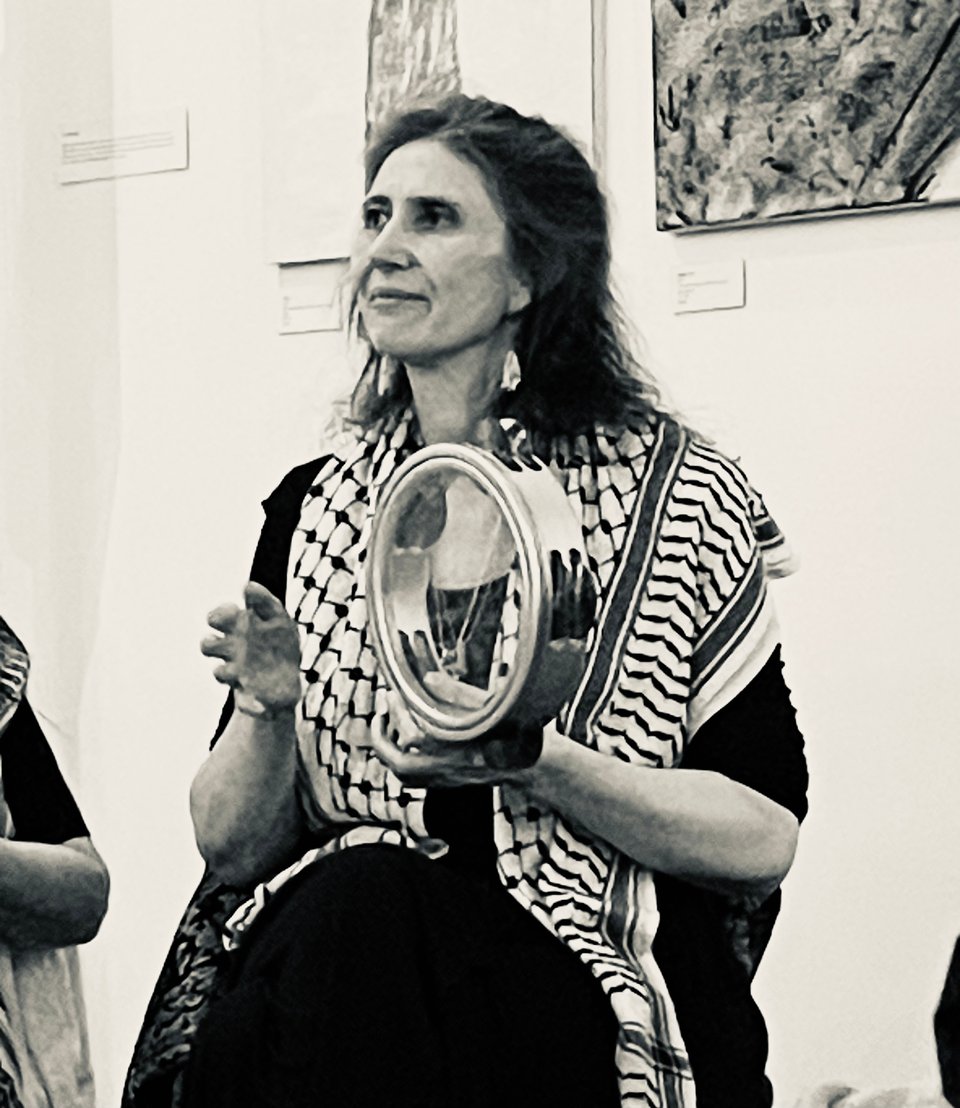 A person in a keffiyeh plays a tambourine