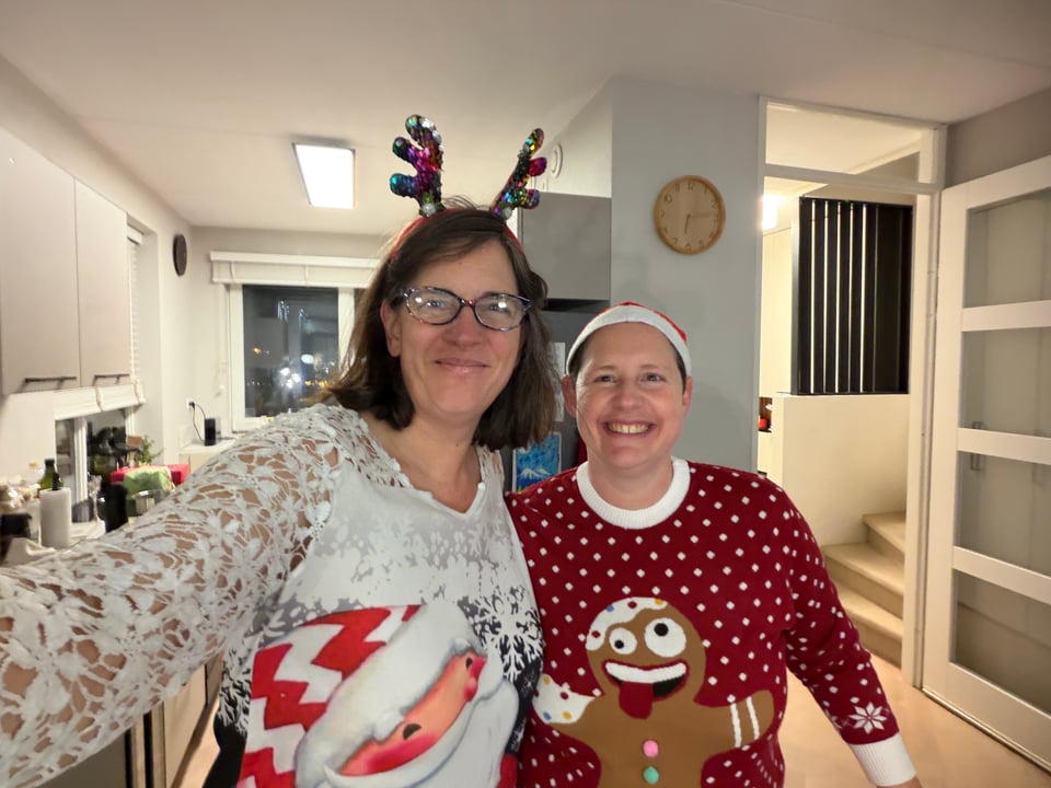 Two women in "ugly" Christmas sweaters smile at the camera.