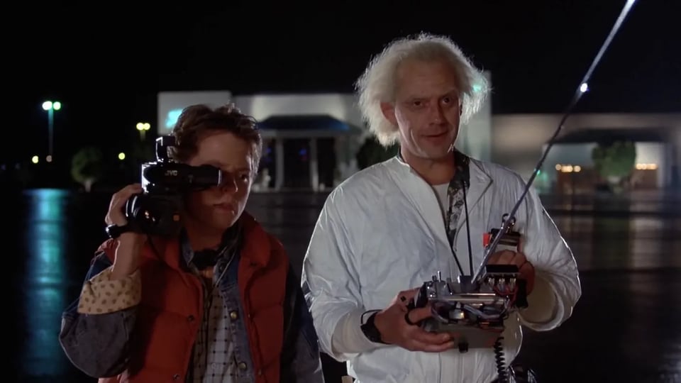 Marty holds a video camera while Doc operates a car by remote control.