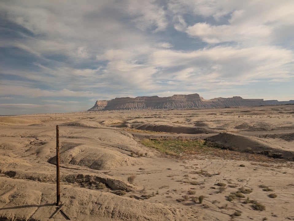 A mesa rising above a mostly dry dirt plain, with a bit of green where a river might seasonally flow.