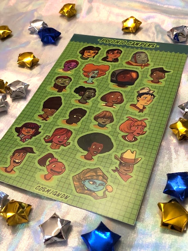 A photo of the Psychic Campers sticker sheet, showing Razputin Aquato and the other campers from the first Psychonauts game. It's on a holographic fabric surface, surrounded by shiny paper stars.