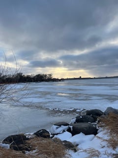 light breaking through beneath big clouds over the lake with rocks in the foreground