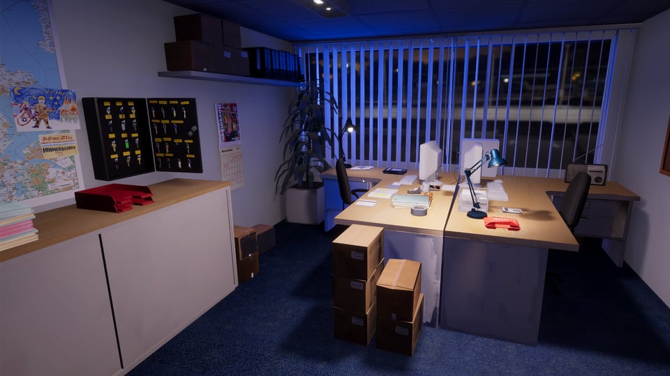 A view of a room in a fire station. Desks in the center, with screens. An open keybox is on the left-side wall next to a map, partly off-frame.