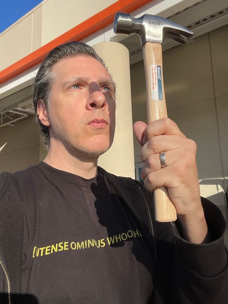 A man holds up a hammer and looks at it with reverence. The sun casts a sharp shadow of the hammer across the man's face