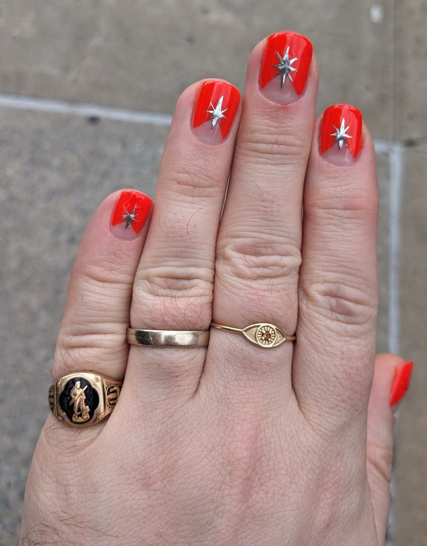 A hand with a manicure showing red french tips and silver starbursts.