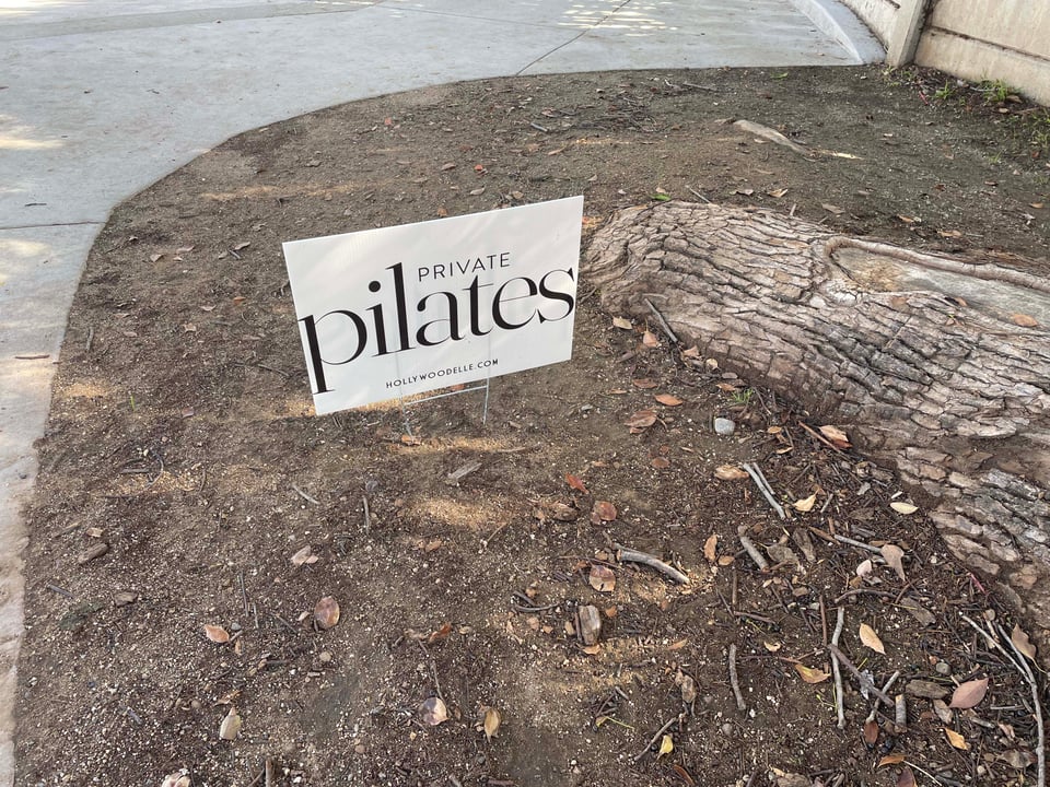 A sidewalk, the base of a tree, and a lawn sign that reads: Private Pilates