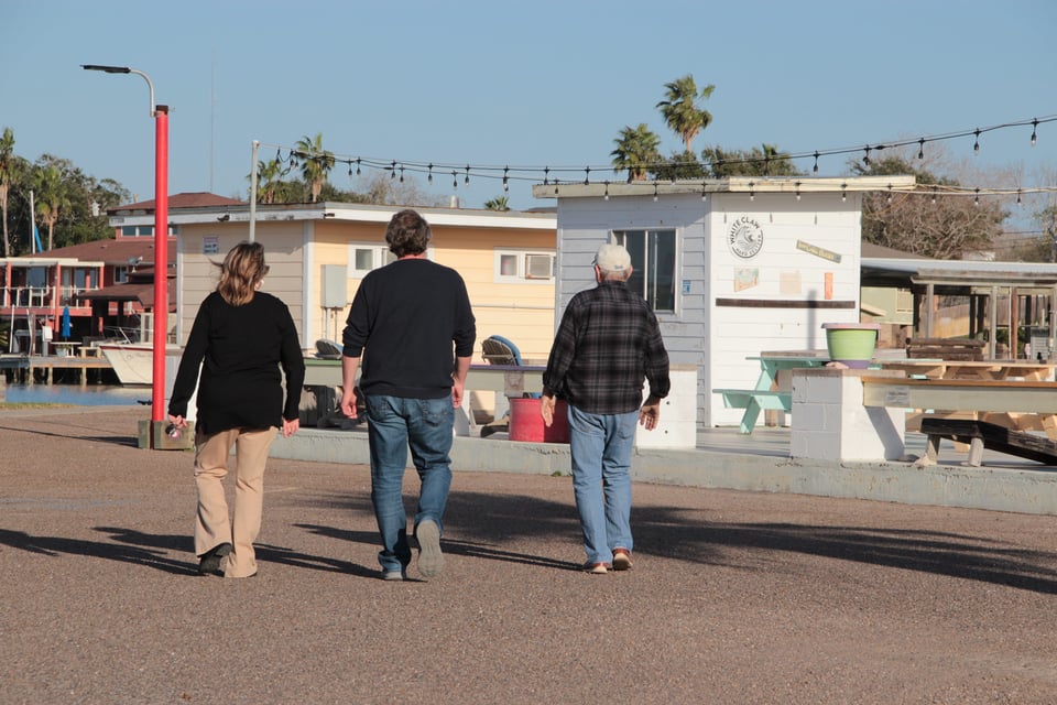 A white woman and two white men walk on the pier, with their backs towards the camera.