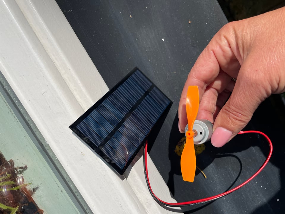 A hand holds a motor with a small orange propeller being powered by a small solar panel.