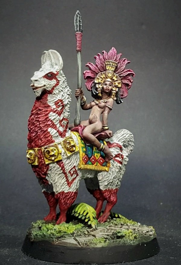 A naked barbarian queen in elaborate headdress sitting astride a giant llama whose coat has been lavishly war-painted.