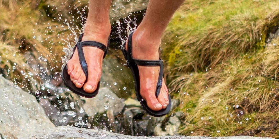 A close-up of feet in sandals leaping with beads of waters splashing.