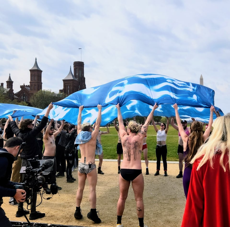 Performance of Etched in Light at the National Mall in DC, with performers lifting a finished cyanotype above their heads in joy and triumph