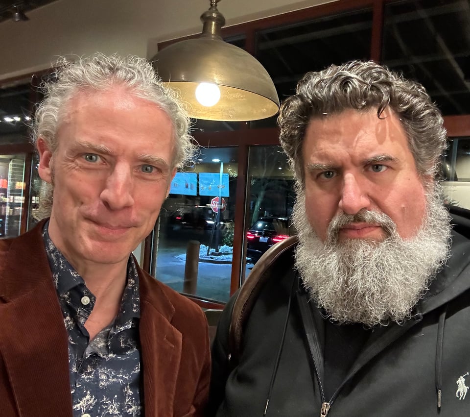 Photo of two white men, one smiling and the other looking serious