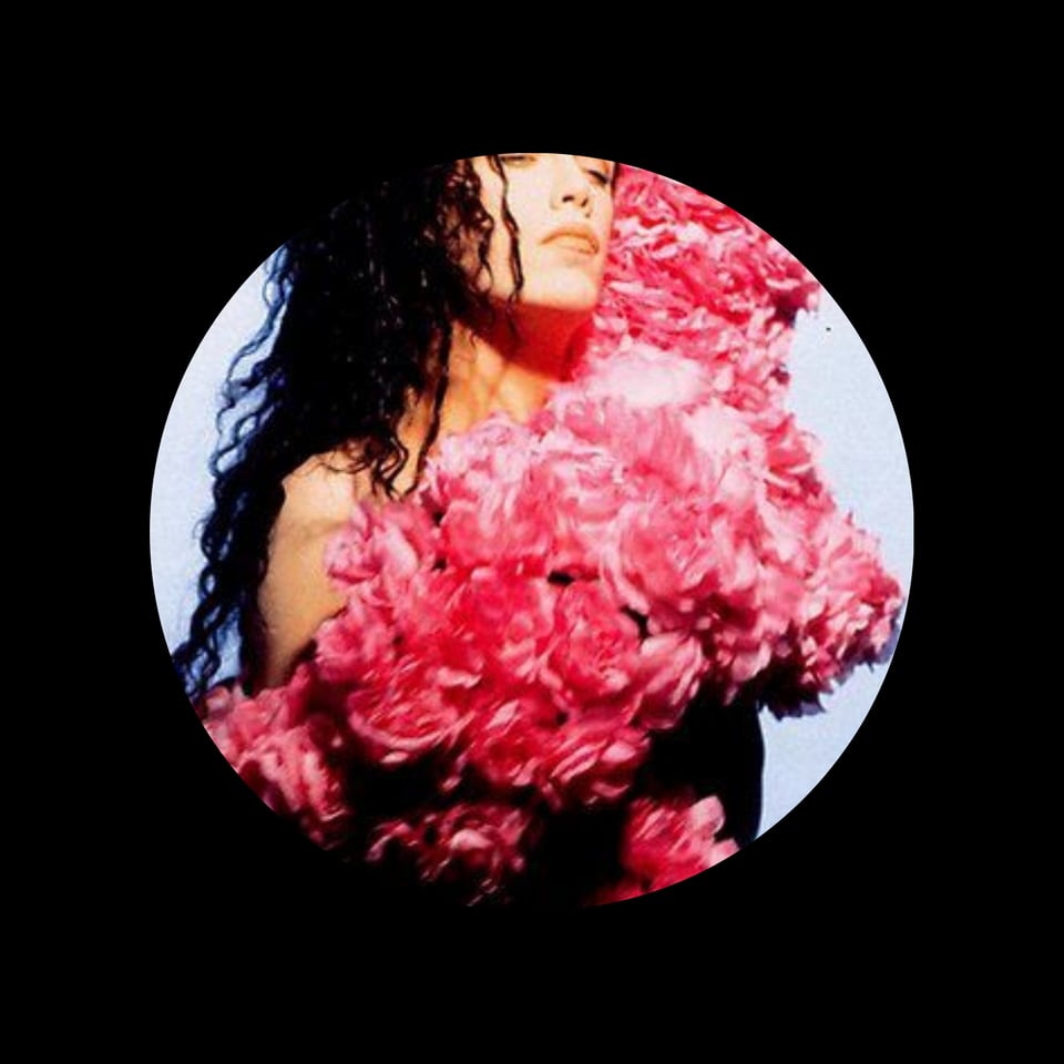 Pete Burns with long curly dark hair, naked but covered by an enormous bunch of pink roses.