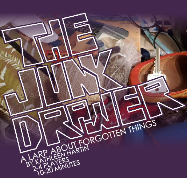 A title reads "The Junk Drawer". Beneath it is written: "A larp about forgotten things, by Kathleen Hartin. Two to four players, 10 to 20 minutes." Behind, a cluttered scene shows junk: a key, a shoe, twine, rocks, dominoes, glasses...