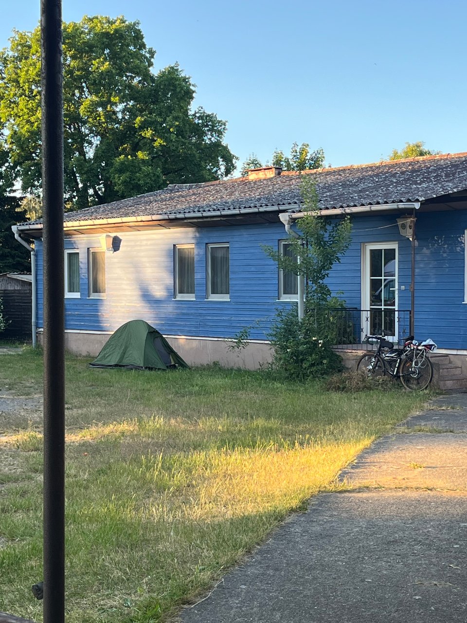 Small green tent next to blue building, and bicycle leaning on small steps up to blue building door.