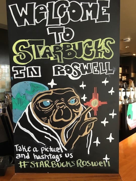 A welcome sign outside the Starucks in Roswell, New Mexico. E.T. has been drawn pointing to the state Zia symbol.