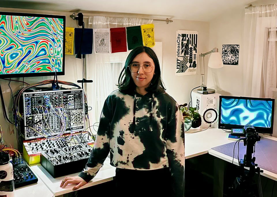 Paloma standing in front of various video equipment in a corner of their studio